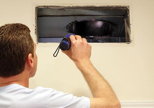 Technician inspecting inside residential ductwork with a flashlight